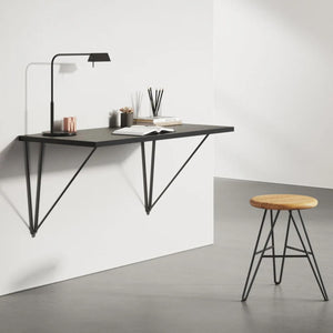 Black wall desk brackets supporting a floating wall desk with stool