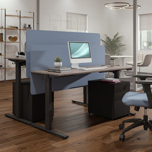 Motorized desk legs supporting a height adjustable office workstation with blue privacy screens and storage pedestal