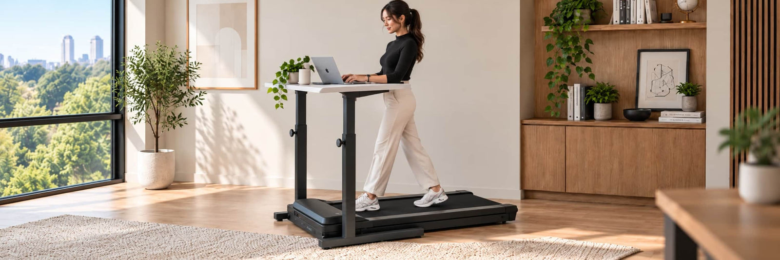 A woman walking on a Savv-e under-desk treadmill beneath a raised standing desk, working at a laptop