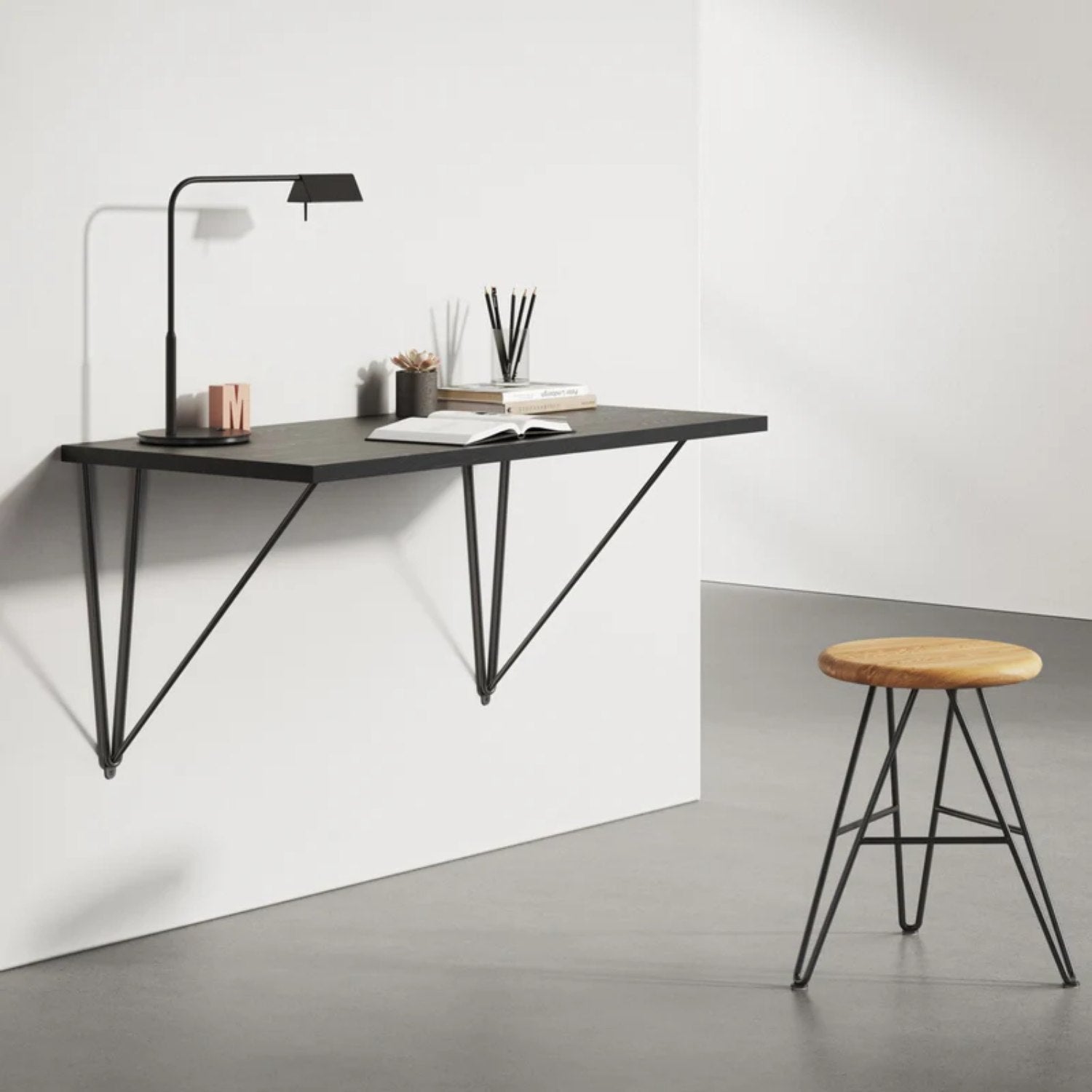 Black wall desk brackets supporting a floating wall desk with stool