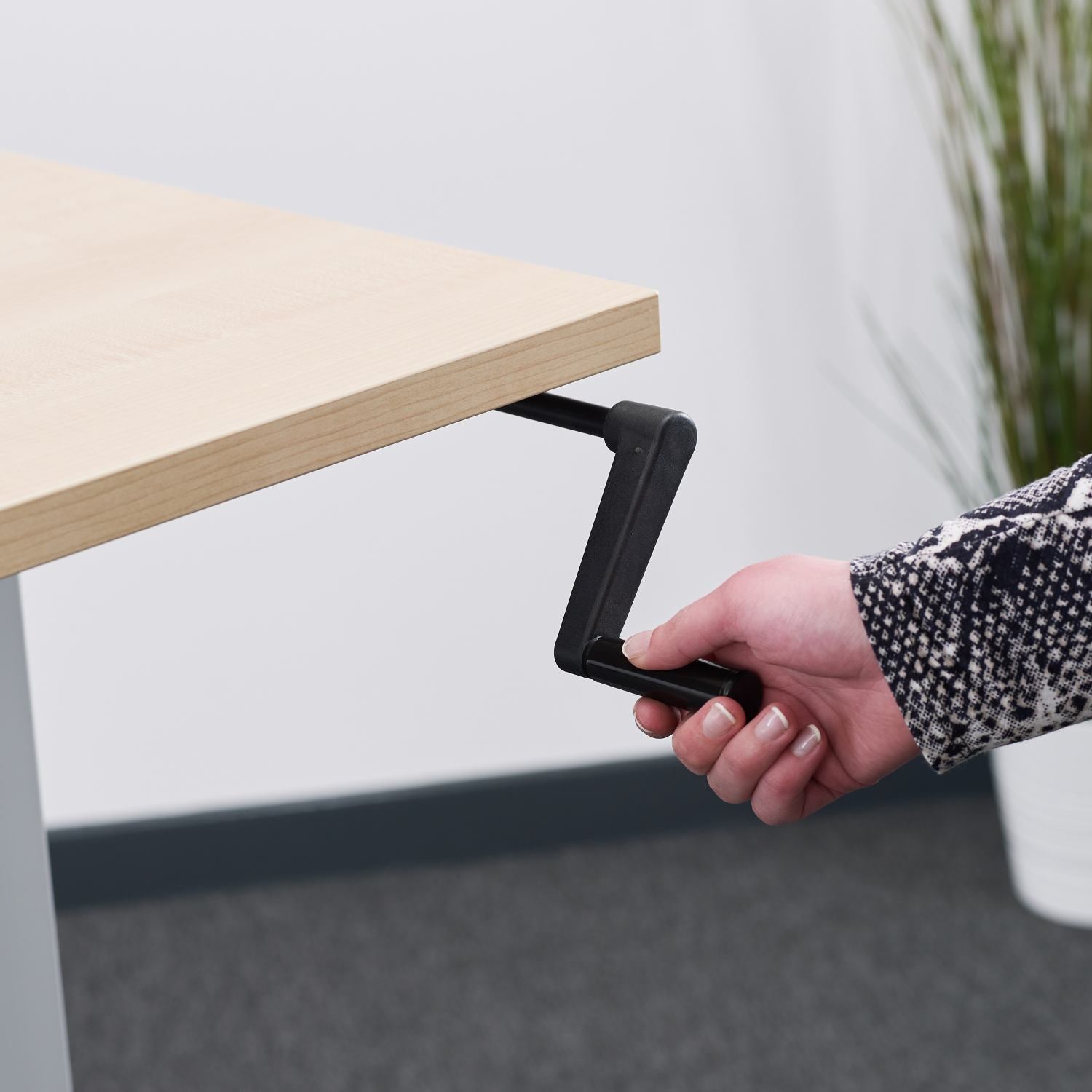 Close-up of a hand using the manual adjustment handle on a hand crank desk