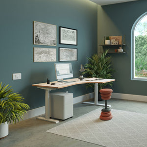 Curved sit stand desk with a light wood desk top and silver frame in a modern home office