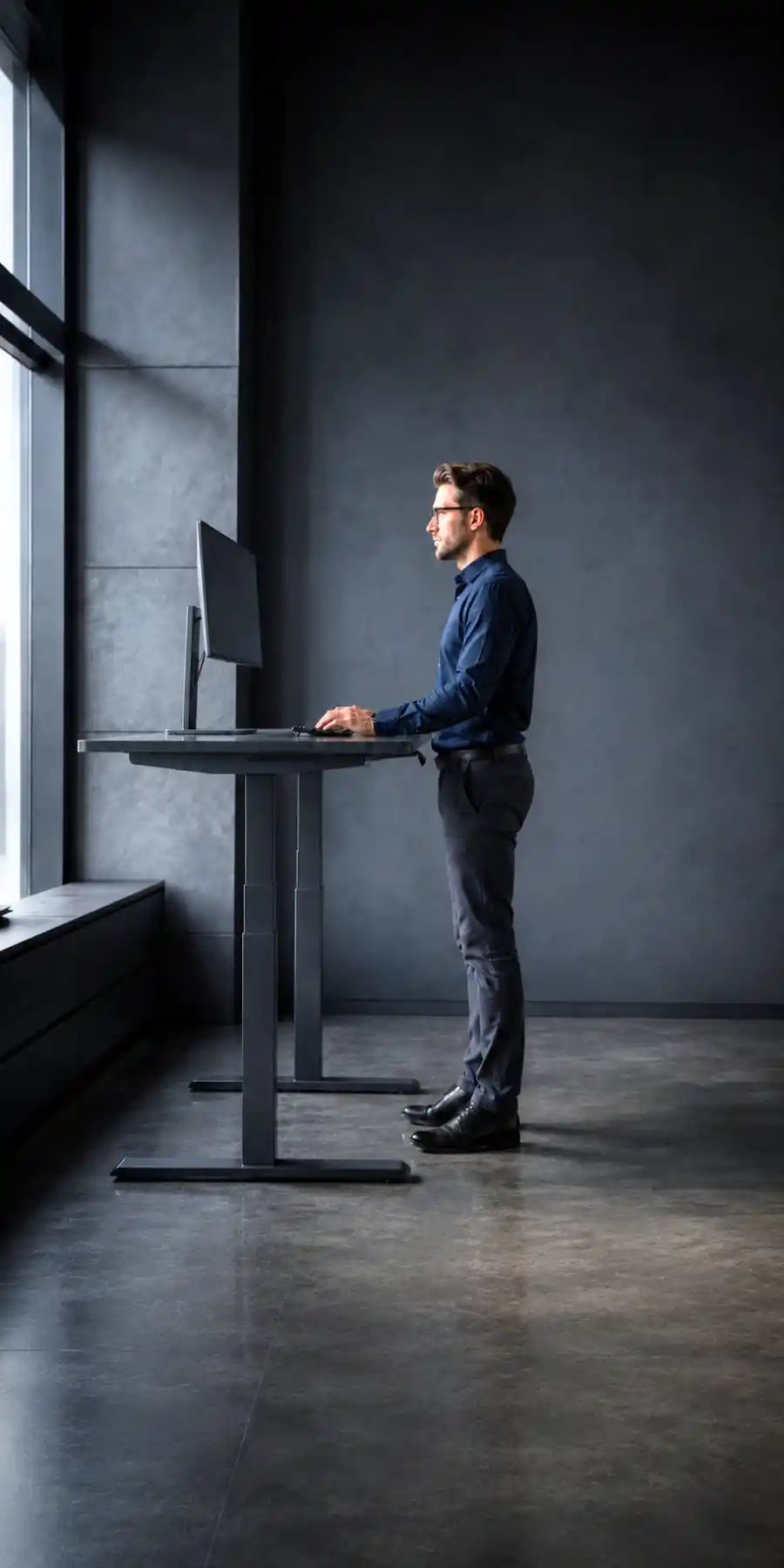 man standing using a height adjustable sit stand desk viewed from the side