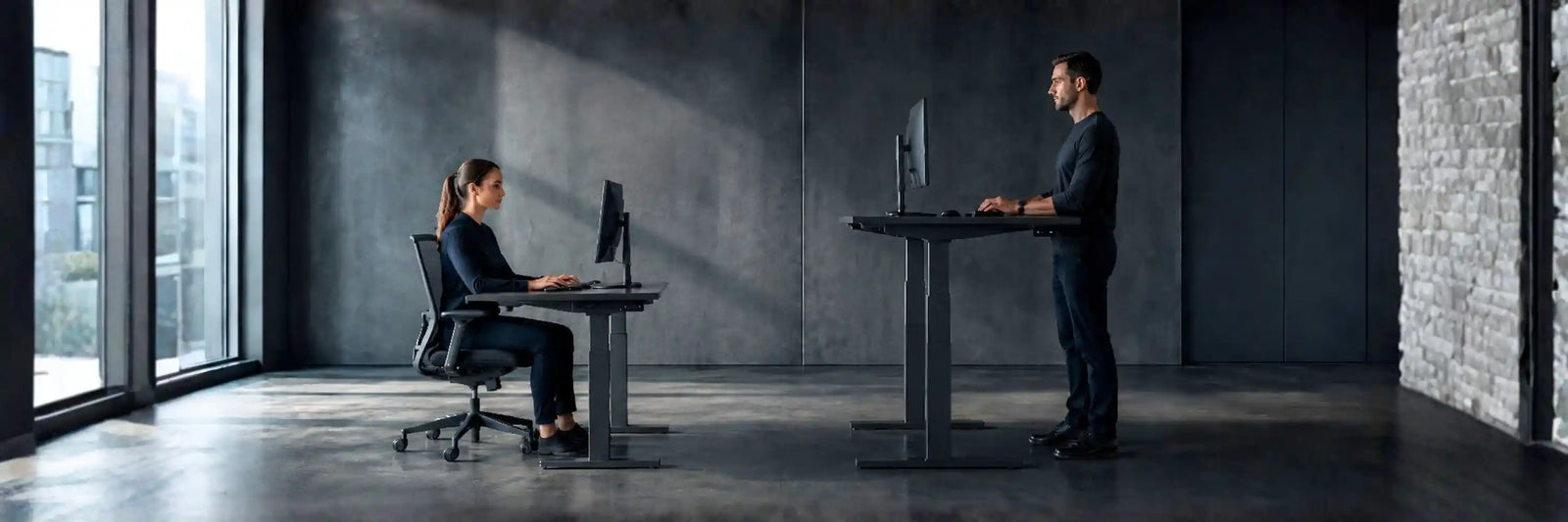 height adjustable standing desks being used by a man in a standing position and a women sitting - viewed from the side